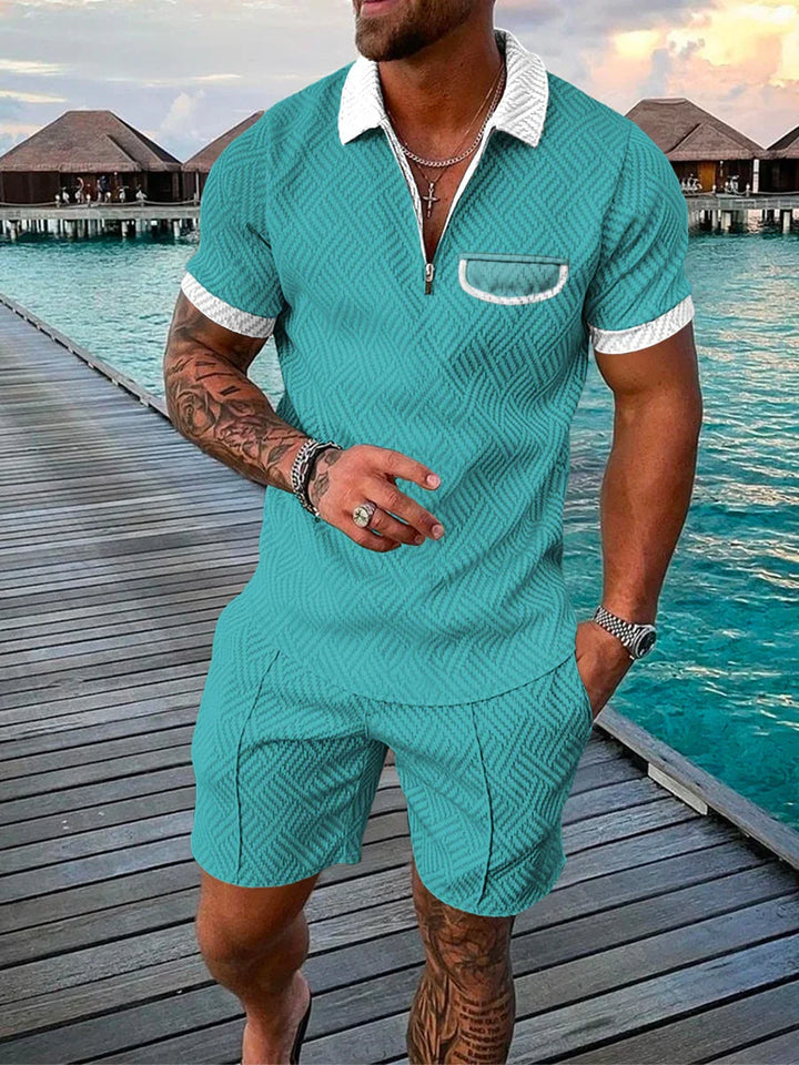 Man wearing teal textured polo shirt and shorts with white collar on wooden pier over turquoise water