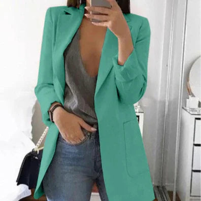 Woman wearing mint green blazer over grey top and blue jeans taking mirror selfie in modern room