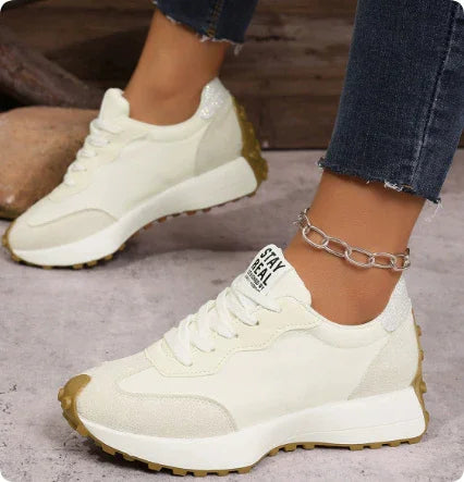 white casual sneakers with textured soles worn with blue jeans and a silver ankle chain on concrete floor