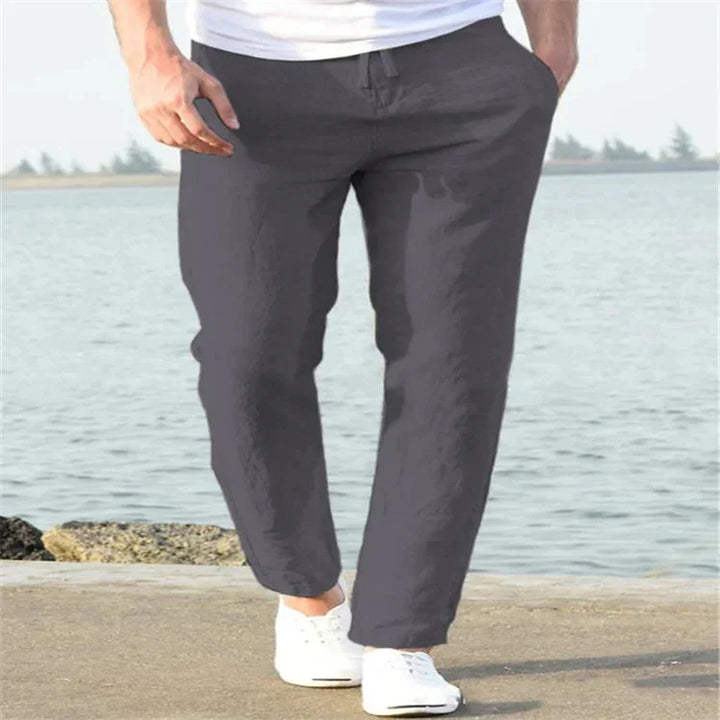 Man wearing black casual pants and white sneakers walking near water on a sunny day