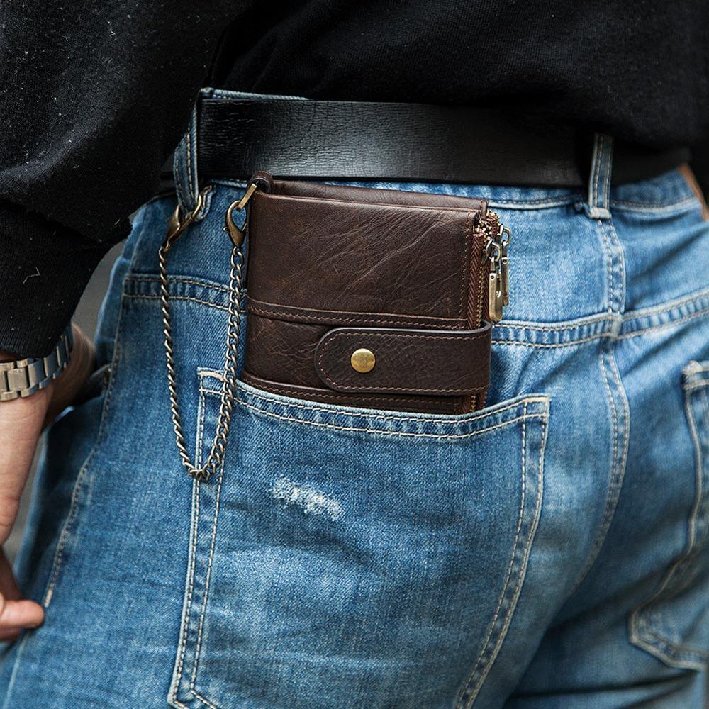 Brown leather wallet with strap and zipper in back pocket of blue denim jeans, black belt, watch