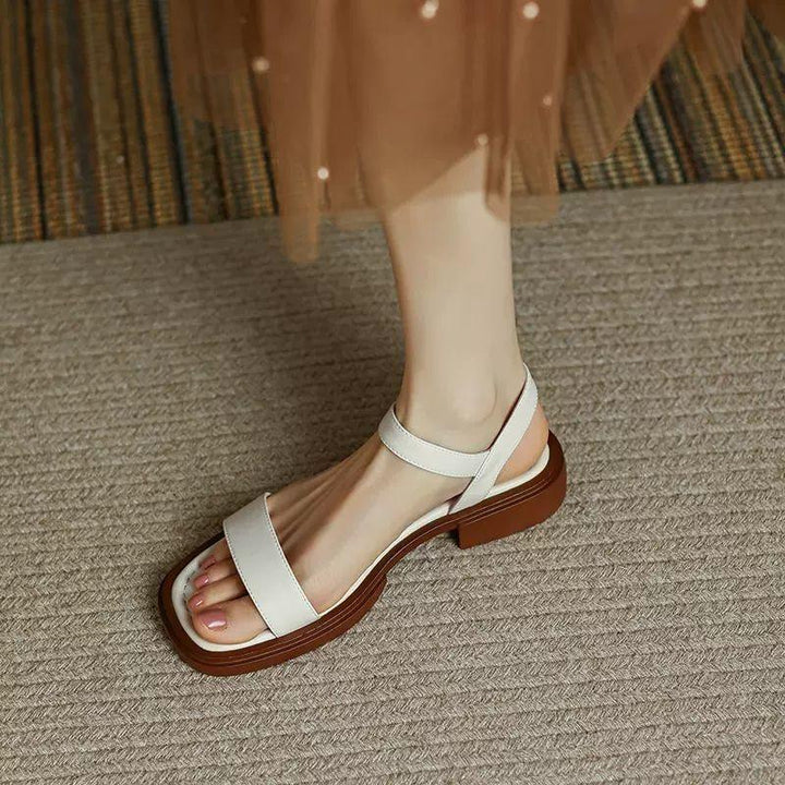 Woman wearing stylish white flat sandals with brown sole on carpeted floor