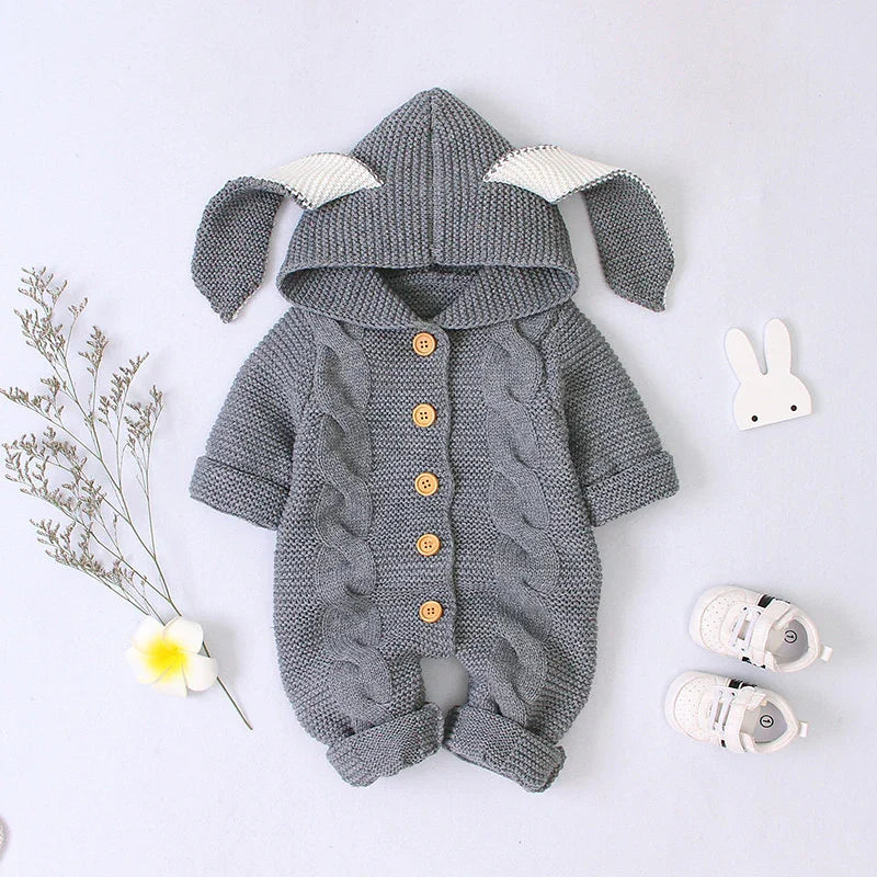 Gray knitted baby romper with bunny ears hood and wooden buttons, styled with white baby shoes and decorative flowers