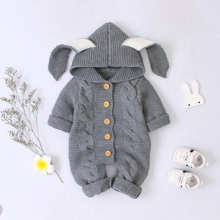 Gray knitted baby romper with bunny ears hood and wooden buttons, styled with white baby shoes and decorative flowers