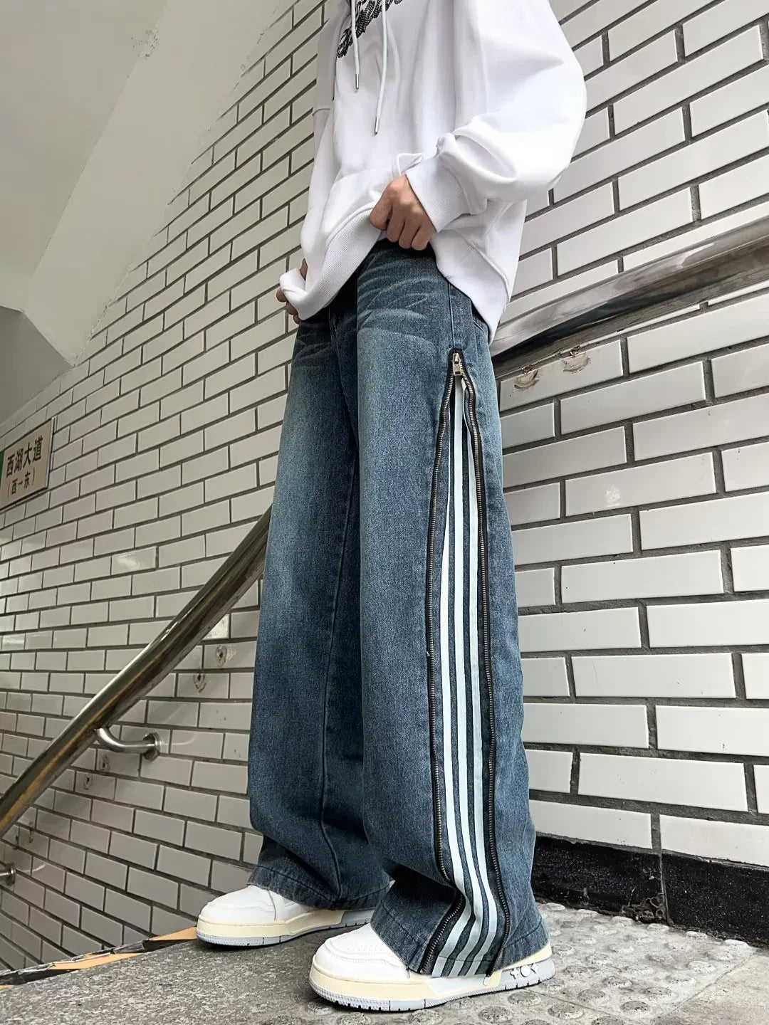 Person wearing white hoodie and wide-leg denim jeans with side zipper stripes, white sneakers