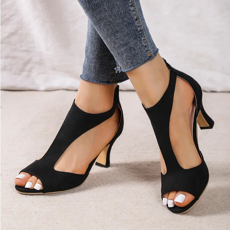 Black open-toe cutout high heel shoes worn with cropped blue jeans on carpet
