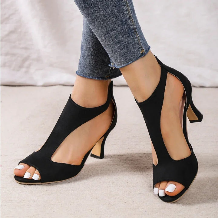 Black open-toe cutout high heel shoes worn with cropped blue jeans on carpet