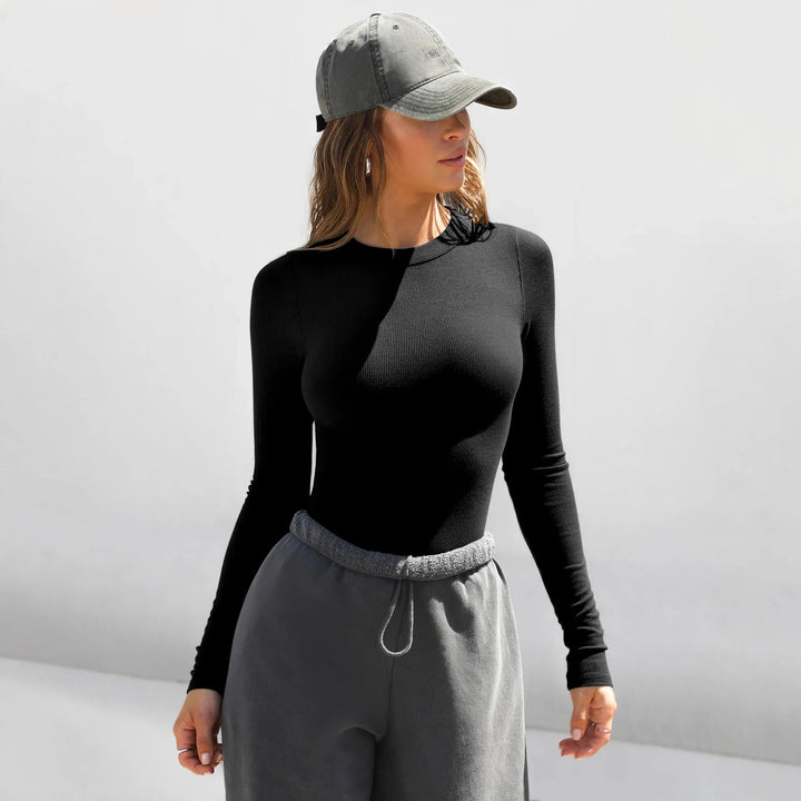 Woman wearing a black long-sleeve top, grey sweatpants, and a grey baseball cap against a white background