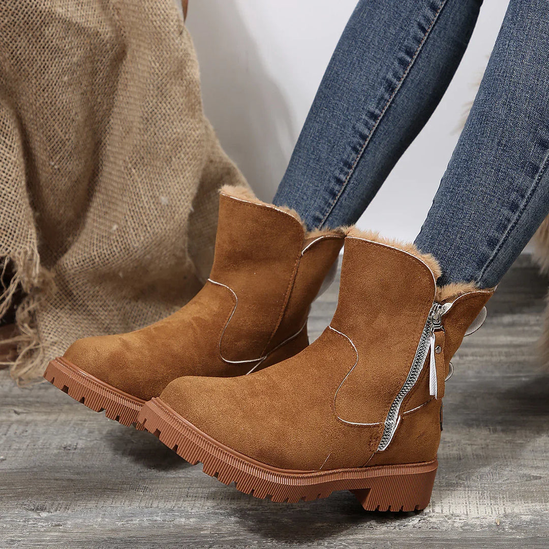 Brown suede ankle boots with fur lining and zipper detail worn with blue jeans on wooden floor
