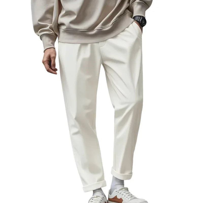 Man wearing beige sweatshirt, white cuffed pants, white socks, and white sneakers with brown accents