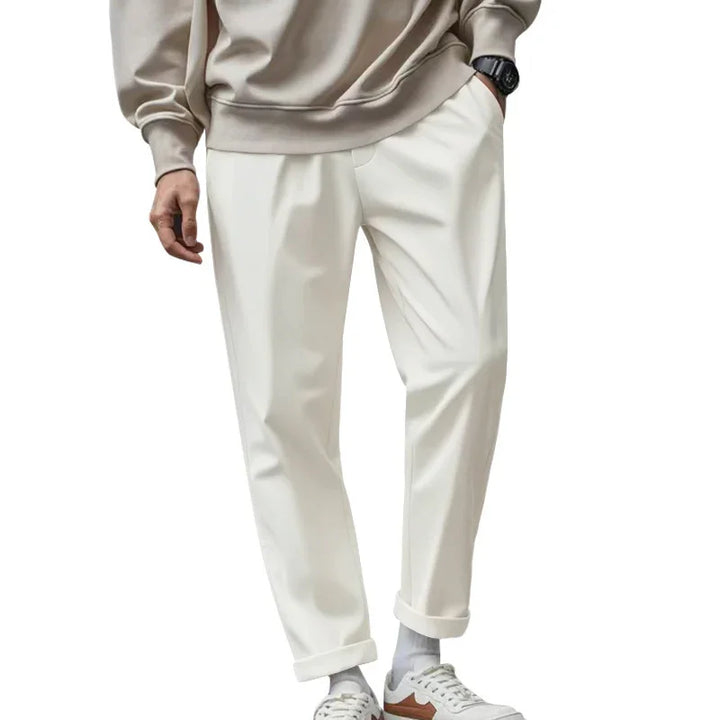 Man wearing beige sweatshirt, white cuffed pants, white socks, and white sneakers with brown accents