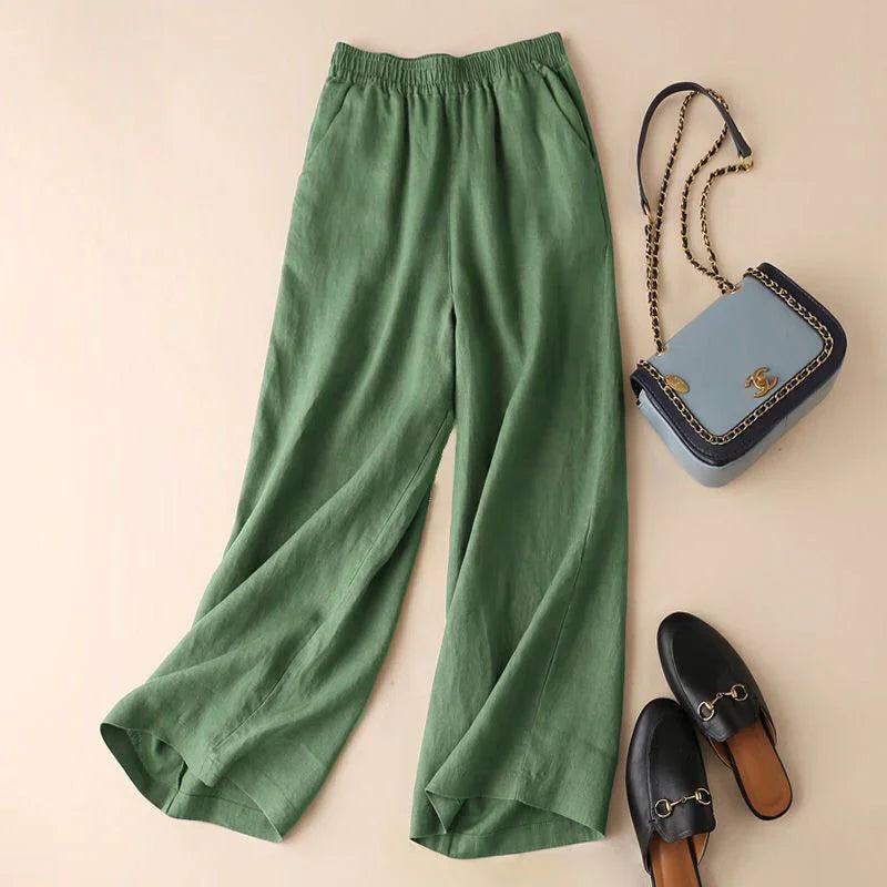 Green wide-leg pants with elastic waistband laid flat next to black slip-on loafers and blue handbag with gold chain