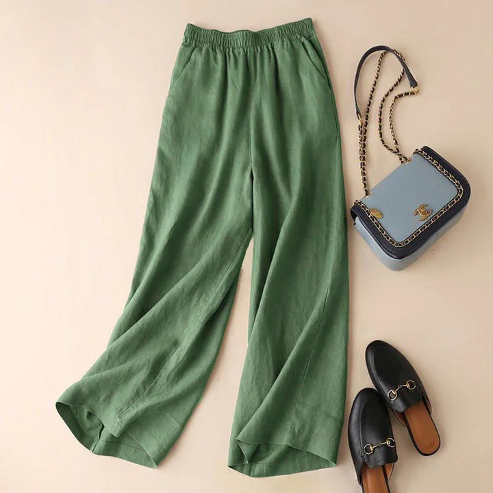 Green wide-leg pants with elastic waistband laid flat next to black slip-on loafers and blue handbag with gold chain