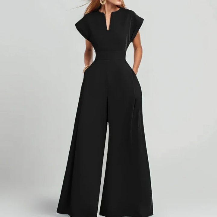 Woman wearing elegant black wide-leg jumpsuit with short sleeves and V-notch neckline on gray background