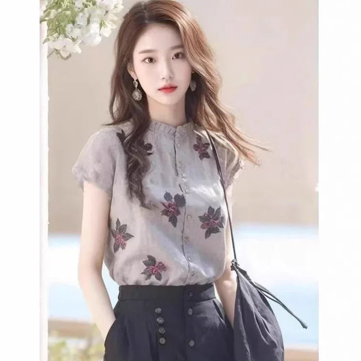 Young woman wearing a floral button-up blouse and high-waisted black pants with a black shoulder bag