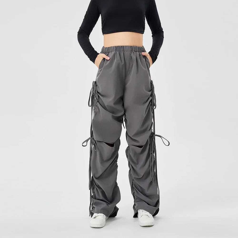 Woman wearing dark gray cargo pants with elastic waist and drawstring details, paired with white sneakers and black cropped top