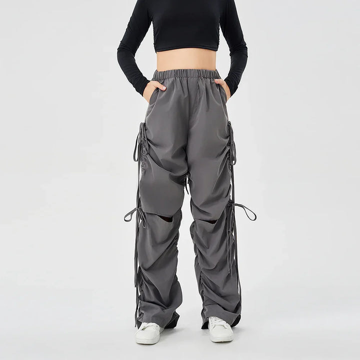 Woman wearing dark gray cargo pants with elastic waist and drawstring details, paired with white sneakers and black cropped top