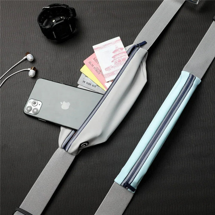 Gray crossbody travel sling bag with phone, cash, cards shown, beside watch and earphones