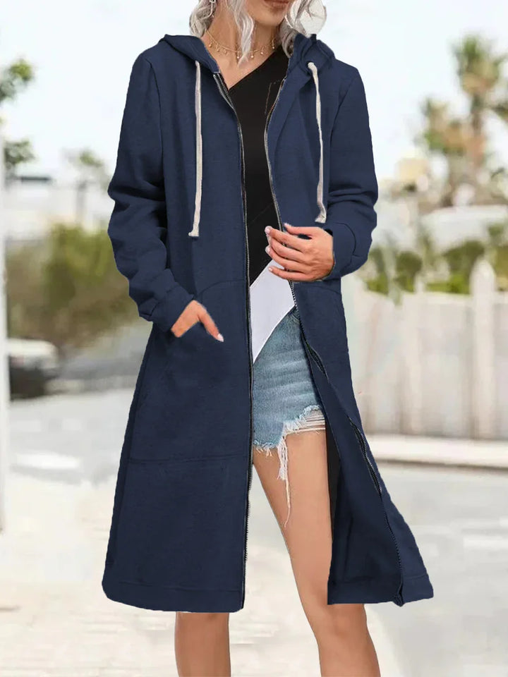 Woman wearing a navy long zip-up hooded coat with white drawstrings and denim shorts outdoors
