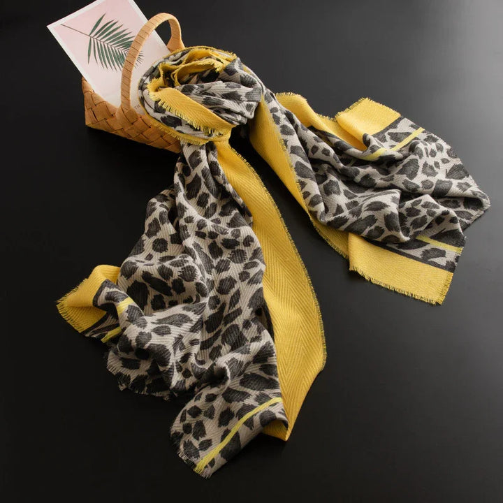 Yellow and gray leopard print scarf with frayed edges draped next to wicker basket and leaf print card
