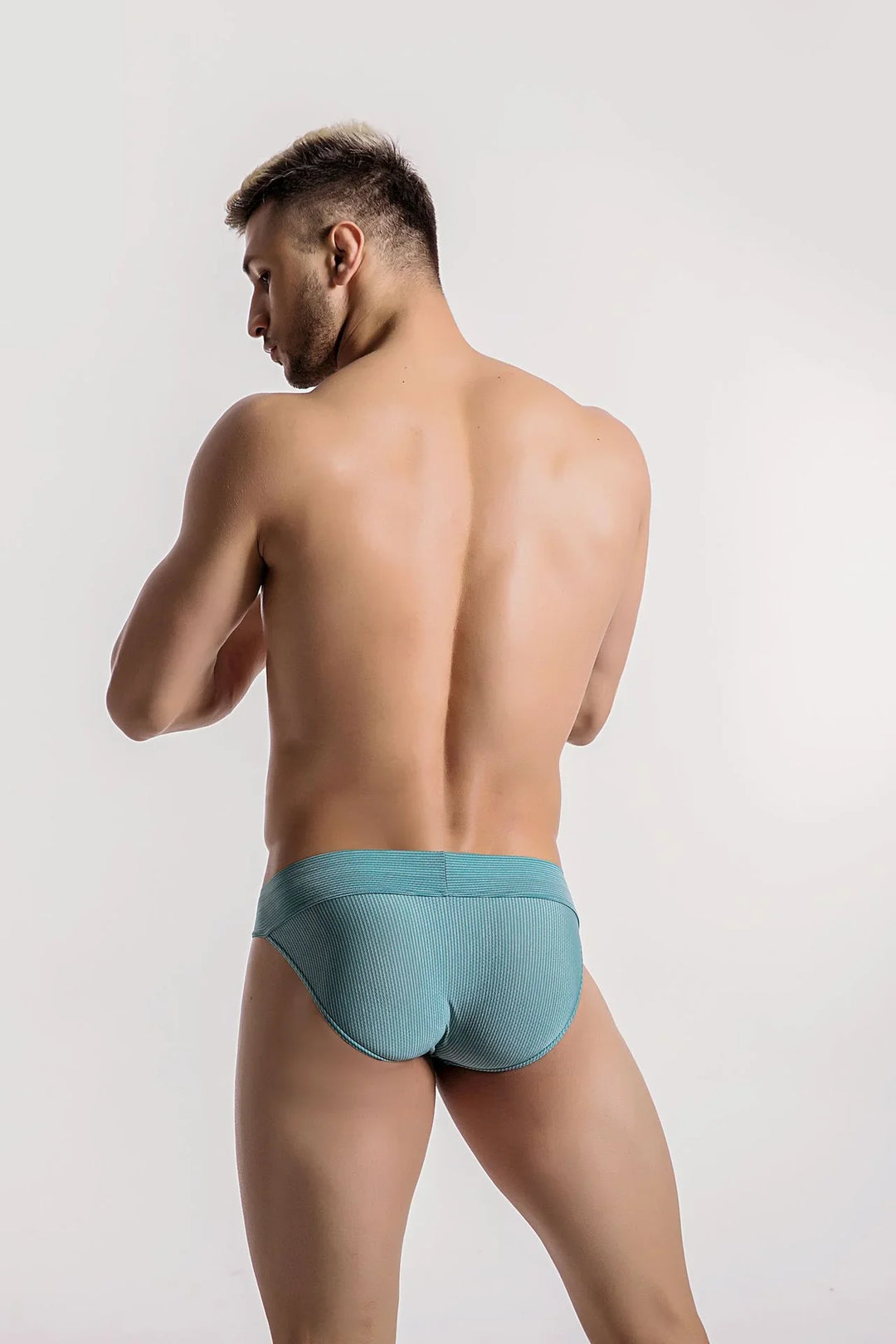 Back view of muscular man wearing ribbed turquoise briefs against a plain white background