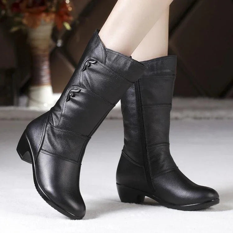 Black mid-calf women's leather boots with low heels and side zipper, worn indoors on carpet