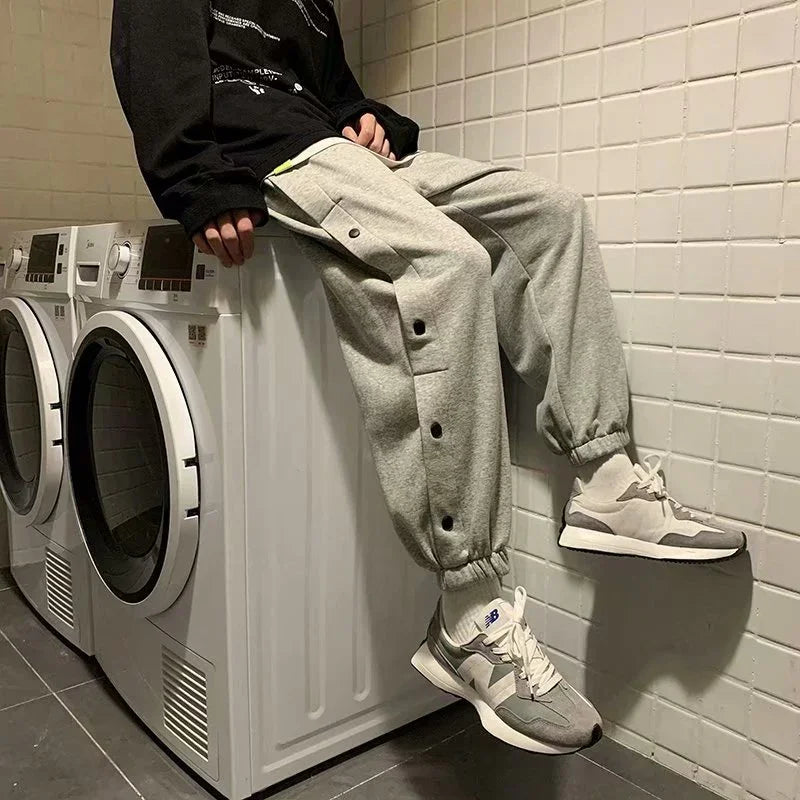 Person in gray jogger pants and New Balance sneakers sitting on a white washing machine in tiled laundry room