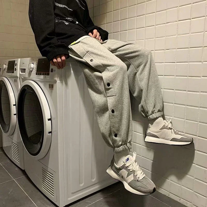 Person in gray jogger pants and New Balance sneakers sitting on a white washing machine in tiled laundry room
