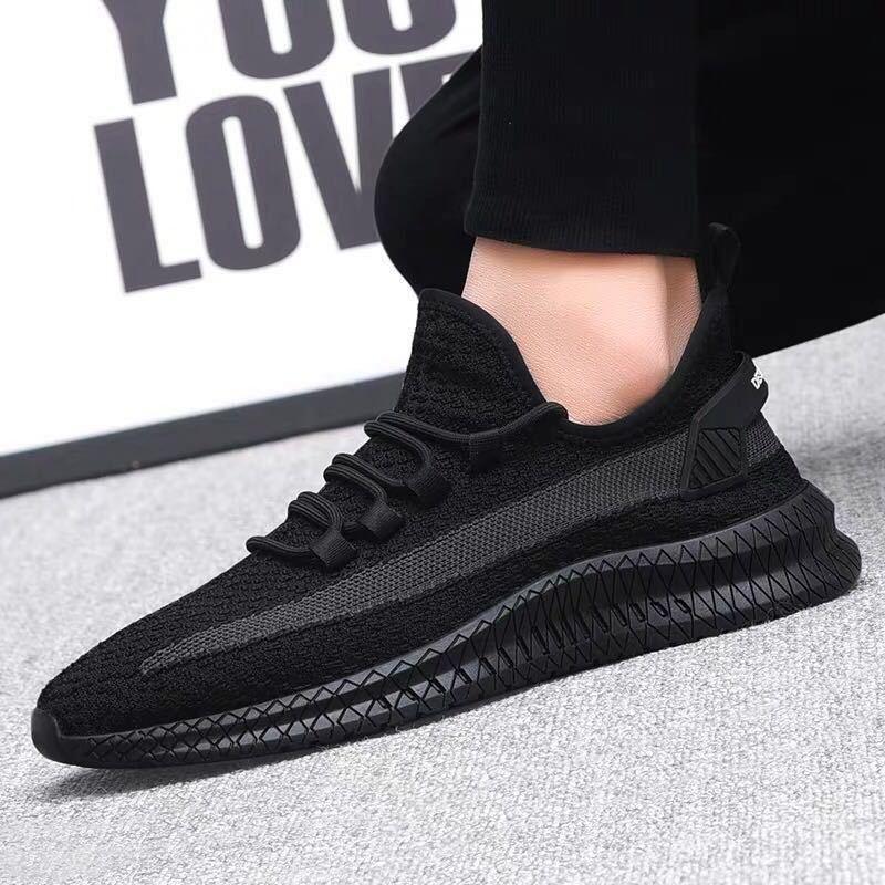 Black knit athletic sneaker with textured sole, worn on foot against gray carpet background