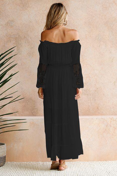 Woman wearing a black off-shoulder maxi dress with embroidered sheer sleeves standing indoors