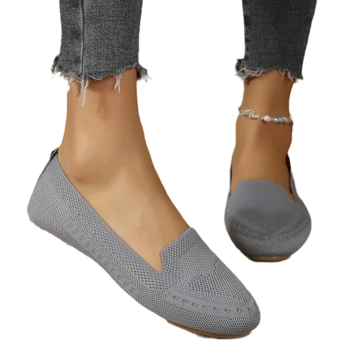 Close-up of feet wearing grey knitted slip-on flats and frayed dark grey jeans with beaded anklet