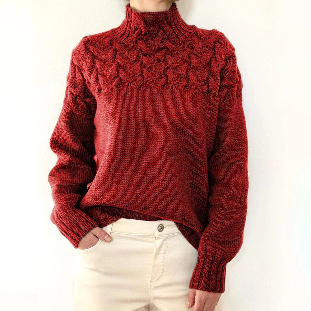 Person wearing a red chunky cable knit turtleneck sweater with cream pants