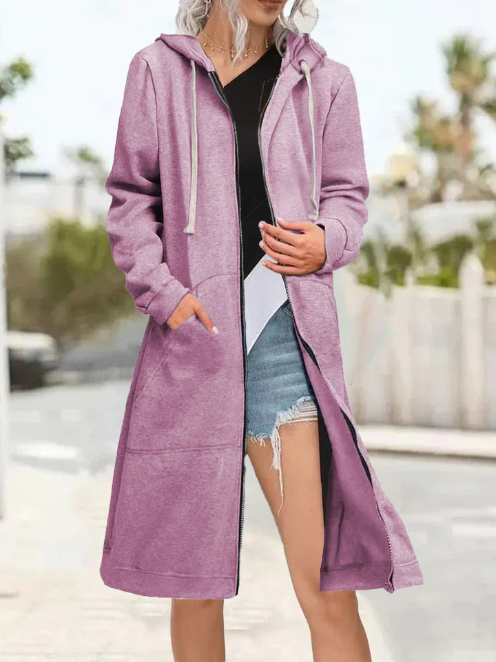 woman wearing long mauve zip-up hooded cardigan with pockets over casual black top and ripped denim shorts outdoors