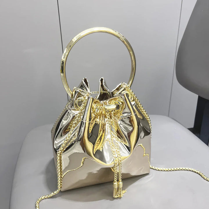 Shiny metallic gold drawstring purse with large circular handle and chain strap on gray chair