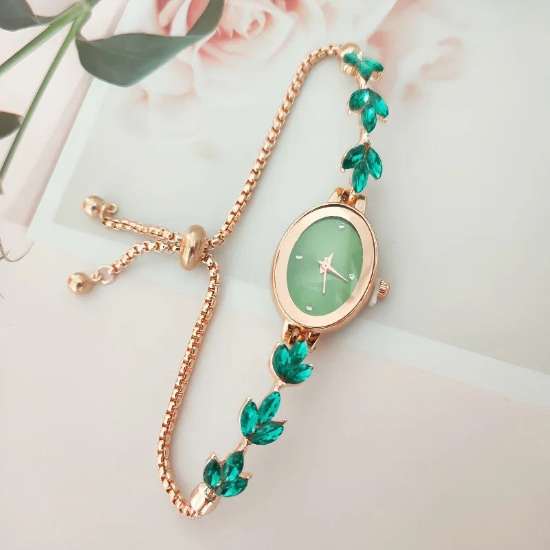 Elegant gold bracelet watch with green leaf-shaped gemstones and green oval dial on a light background
