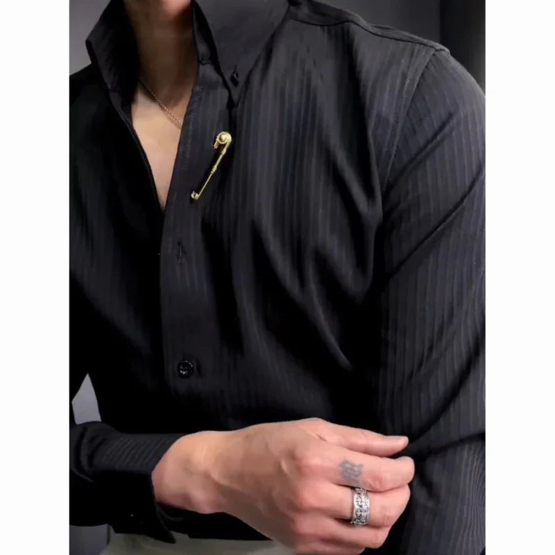Man wearing black pinstripe shirt with gold safety pin brooch and silver rings on hand