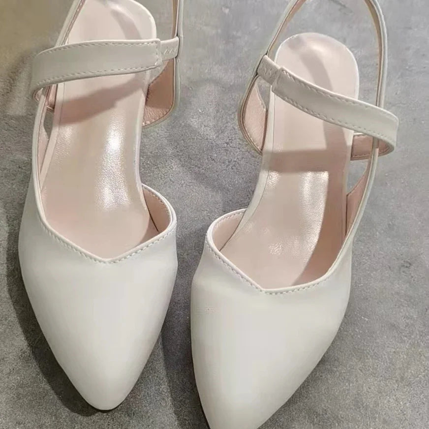 Pair of white pointed toe slingback flats with low heels on gray surface