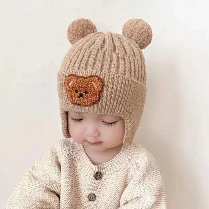 Toddler wearing beige knit hat with bear ears and bear patch, cream knit sweater, white background