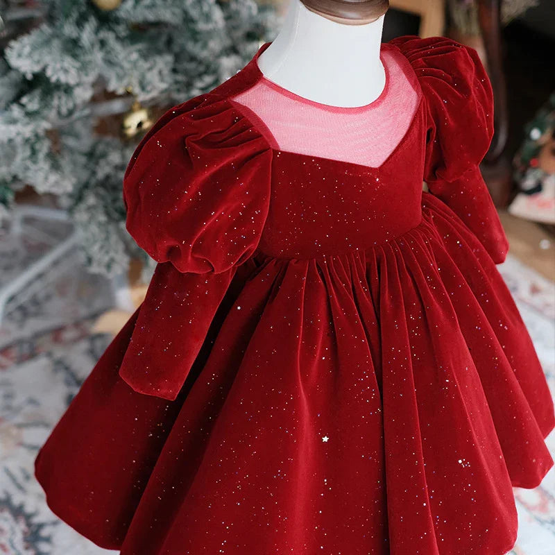 Red velvet toddler dress with puffed sleeves and glitter details on mannequin near Christmas tree