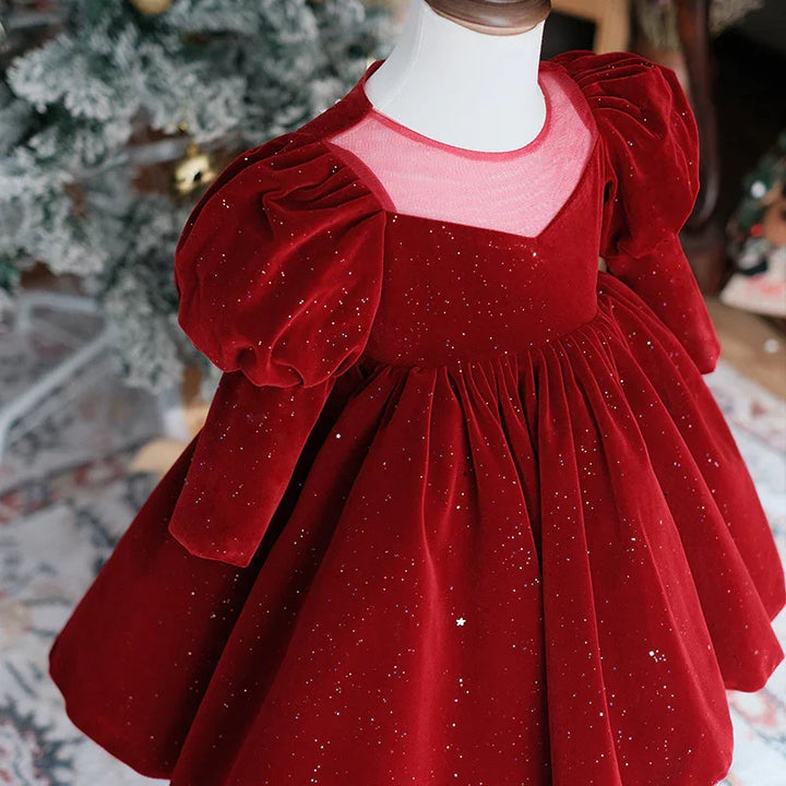 Red velvet toddler dress with puffed sleeves and glitter details on mannequin near Christmas tree