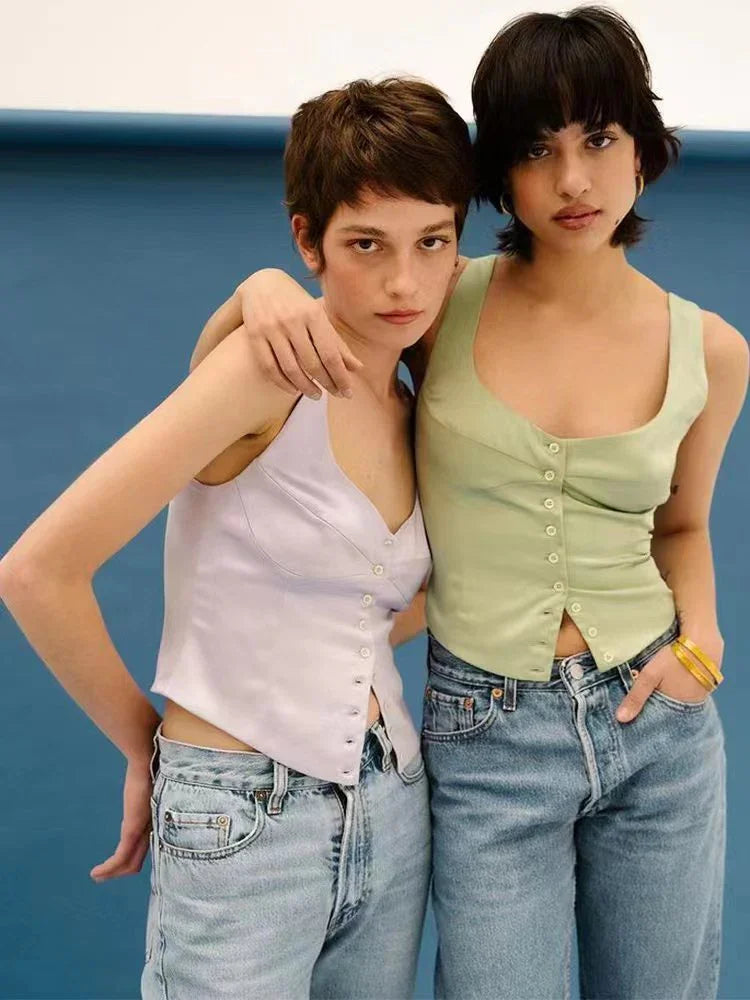 Two young women wearing pastel buttoned tank tops and light blue jeans posing against a blue background