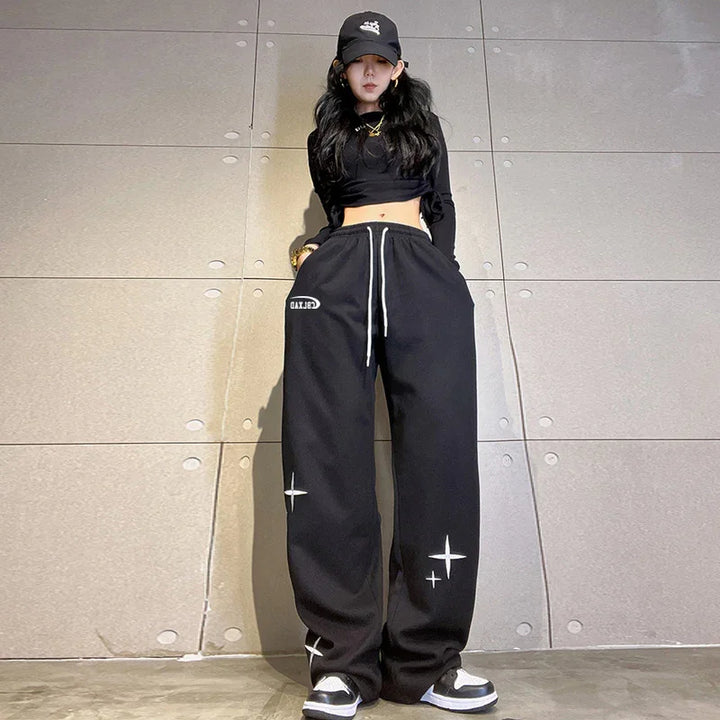 woman wearing black crop top, black baseball cap, and black wide-leg sweatpants with white star designs