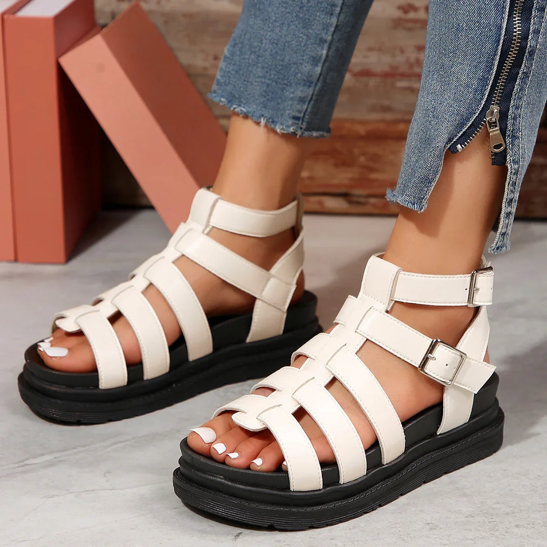White strappy platform sandals with buckle details worn with cropped blue jeans on concrete floor