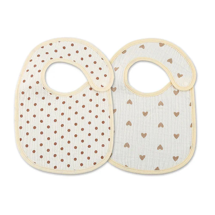 Two baby bibs with beige trim, one with brown polka dots and the other with brown heart patterns