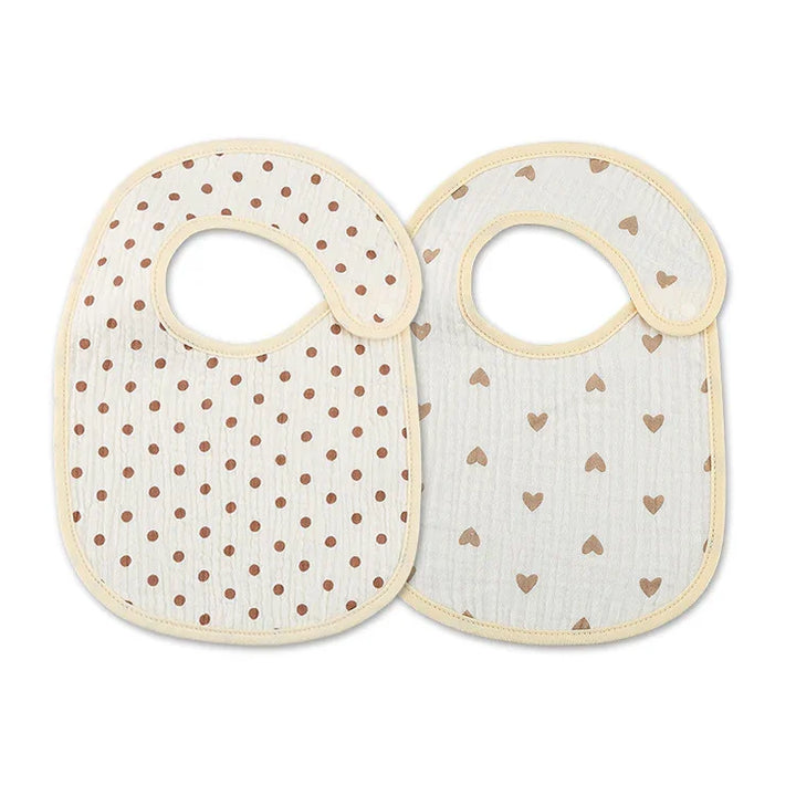 Two baby bibs with beige trim, one with brown polka dots and the other with brown heart patterns