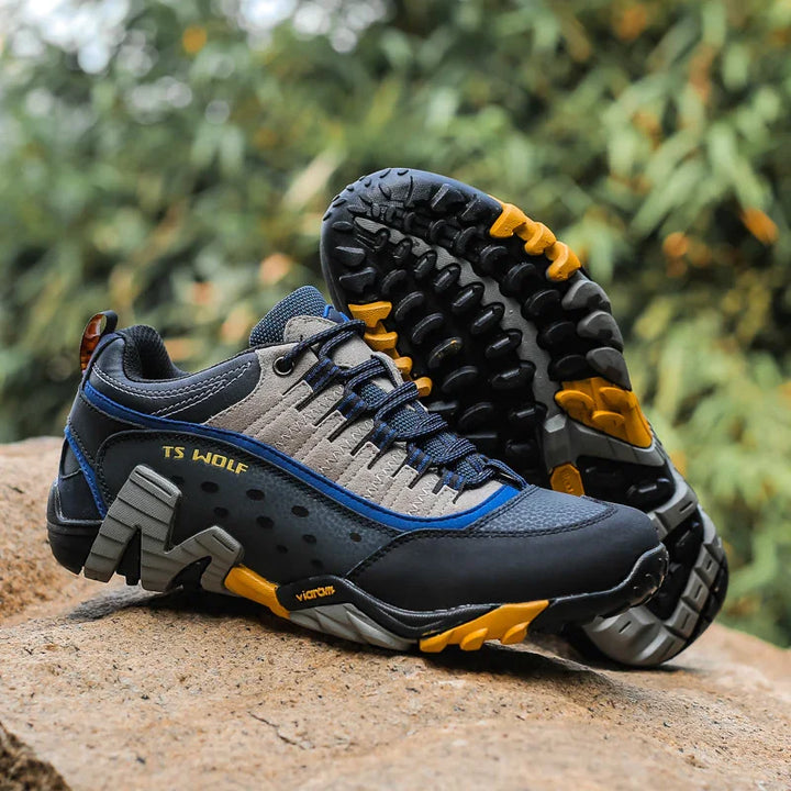 TS Wolf hiking shoes in gray, black, blue, and yellow with rugged Vibram soles on a rock