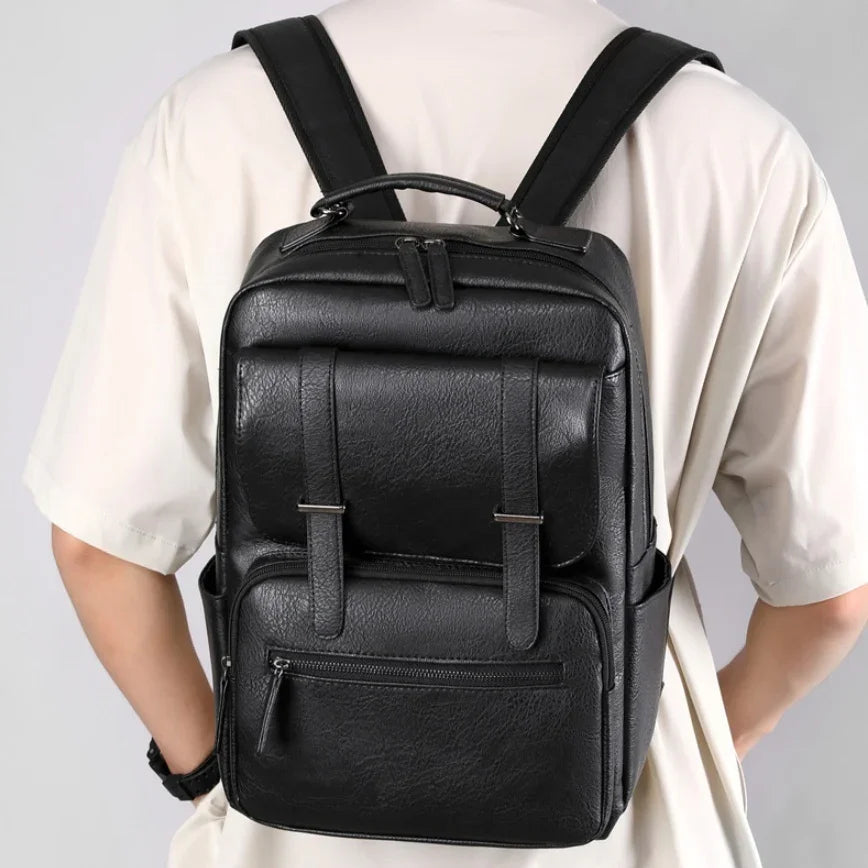 Black leather backpack with front pockets and straps worn by person in white shirt