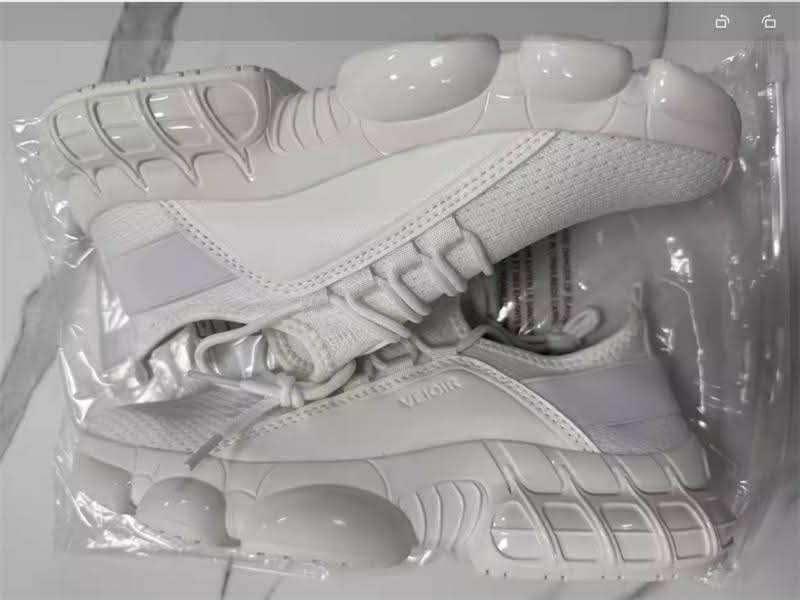 Pair of white athletic sneakers with unique bubble and grid sole design packaged in clear plastic