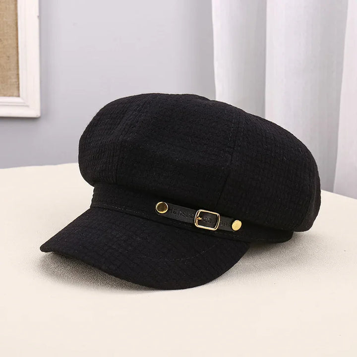 Black textured newsboy cap with gold buckle detail on a light surface