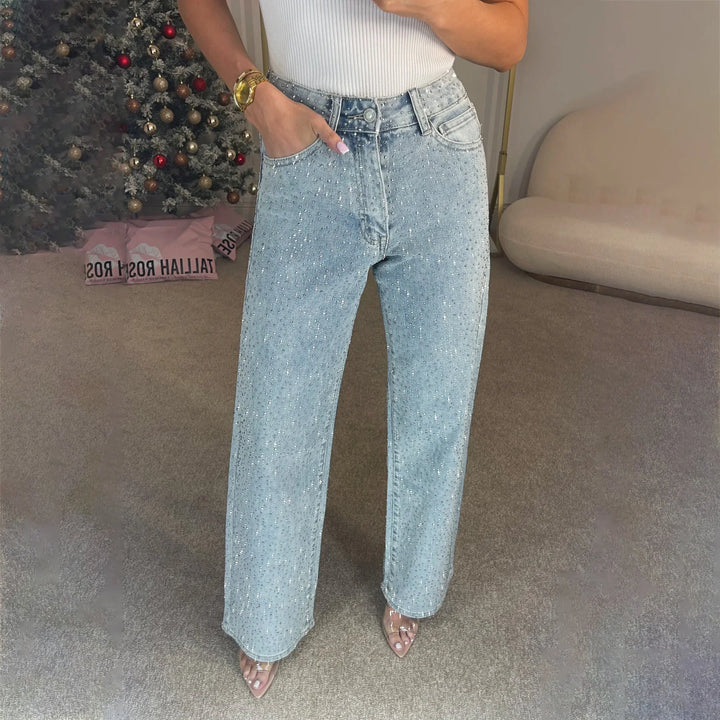 Woman wearing light blue high-waisted jeans embellished with small rhinestones, standing indoors near a decorated Christmas tree
